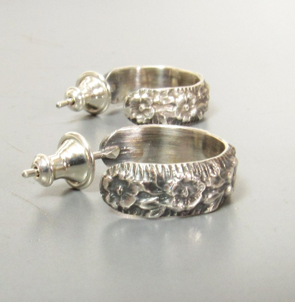 A pair of sterling silver post back hoop earrings with a floral design. The earrings have a polished finish.