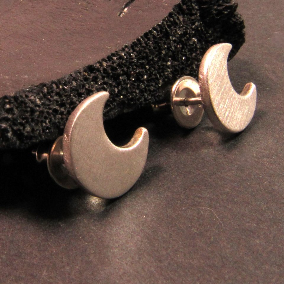 A pair of silver crescent moon stud earrings. The earrings are made of sterling silver and have a simple, modern design.