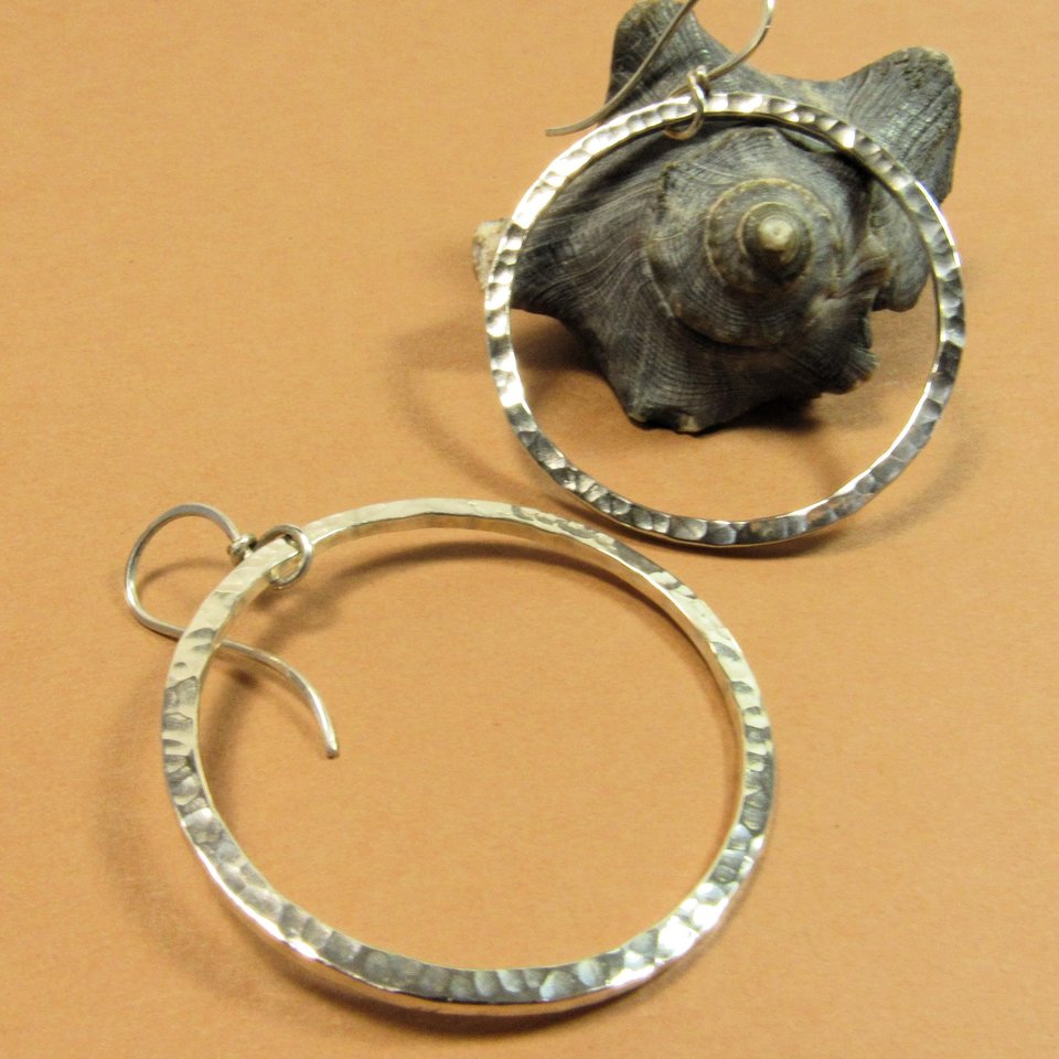 Hammered loops of thick sterling silver wire make for a glamorous statement pair of earrings. Polished bright for reflection from the almost faceted appearance of hammer marks. 2 iches tall x 1 and 5/8 inches wide.