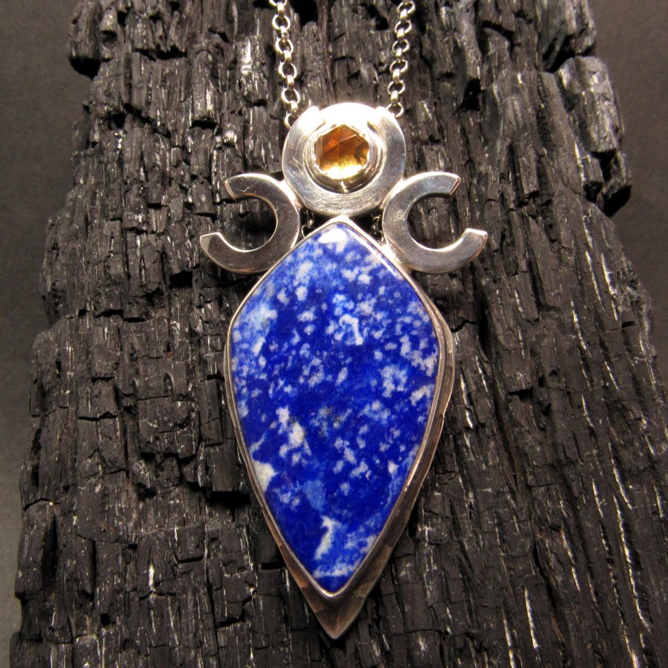 Triple goddess / moon pendant necklace with a faceted citrine and large lapis lazuli cabochon crafted from argentium sterling silver, fine silver. Pendant measures 2 inches from the top and is 7/8 inch across widest part and is suspended on a 18 inch sterling silver chain. Displayed against charred wood.