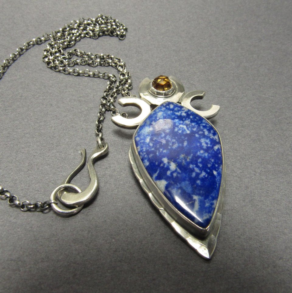 Triple goddess / moon pendant necklace with a faceted citrine and large lapis lazuli cabochon crafted from argentium sterling silver, fine silver. Pendant measures 2 inches from the top and is 7/8 inch across widest part and is suspended on a 18 inch sterling silver chain. Close up of clasp. Displayed on grey background.