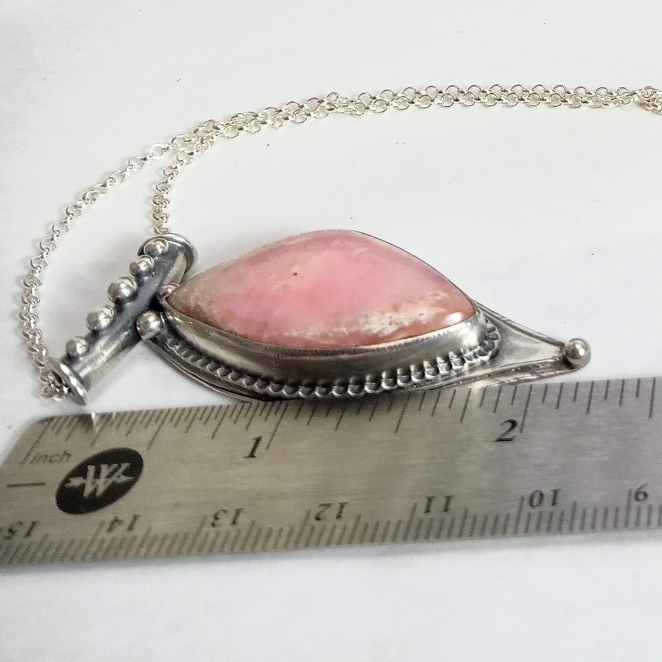 Soft elegance meets artisan craftsmanship in this one of a kind handcrafted pendant featuring a beautifully pastel pink opal set in textured Argentium® sterling silver. The unique, petal-shaped stone in a petal shaped setting radiates gentle warmth in a soothing blush hue—perfect for those who adore subtle statement pieces with soulful charm. 2.25" long x 7/8" wide.
