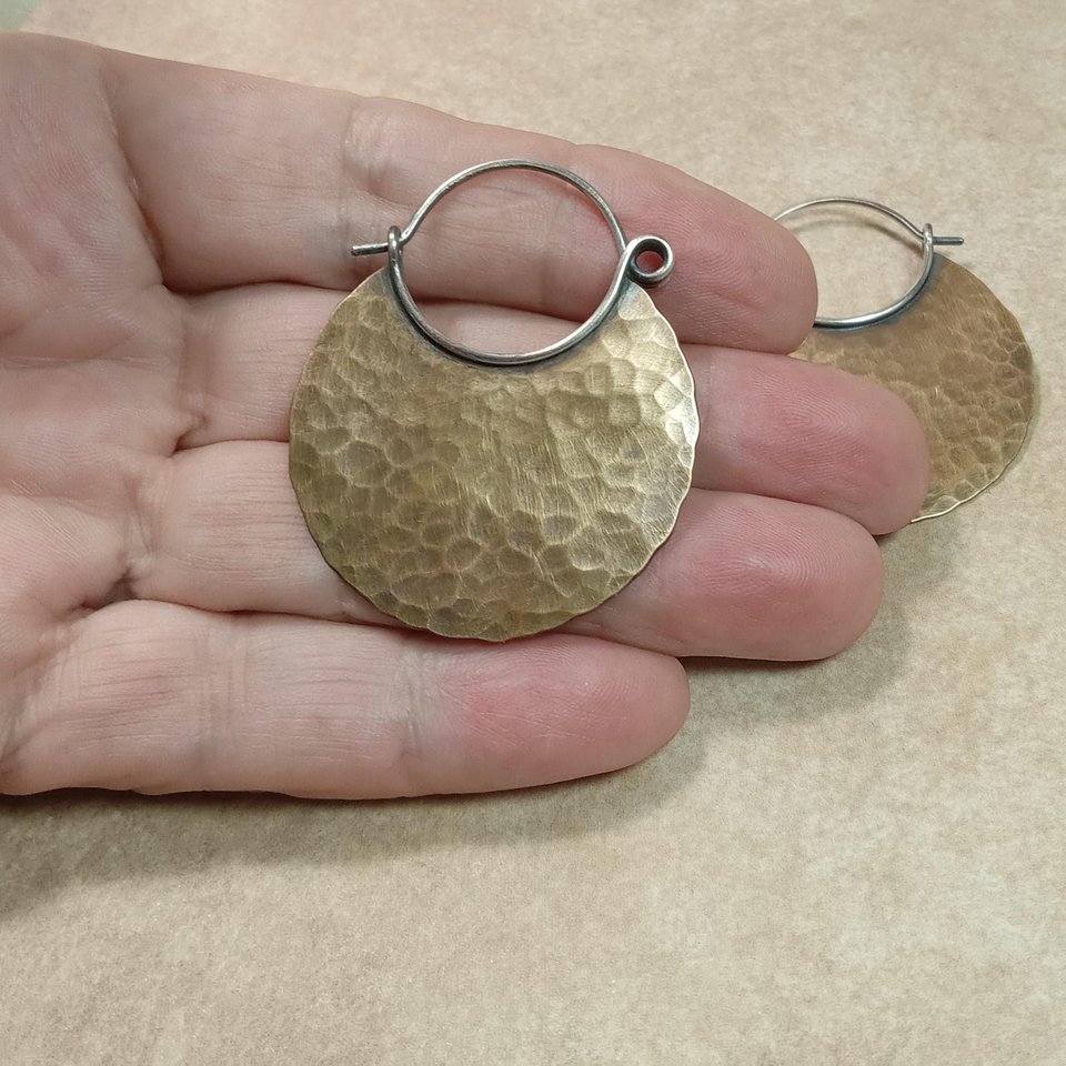 Photo in hand of large mixed metal hammered hoop earrings.