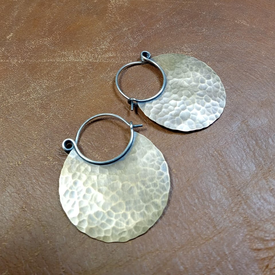 Large hammered mixed metal hoop earrings on leather background.
