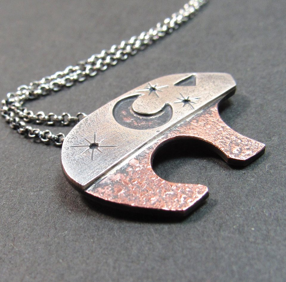 Handcrafted Ursa bear necklace in sterling silver and copper, with celestial moon and star cutouts, smooth flowing sterling silver bail, and sturdy 18 inch sterling chain with handmade findings. Bear measures 3/4 tall x 1.25" wide. Sterling silver chain and handmade findings complete the necklace. Displayed on grey background.
