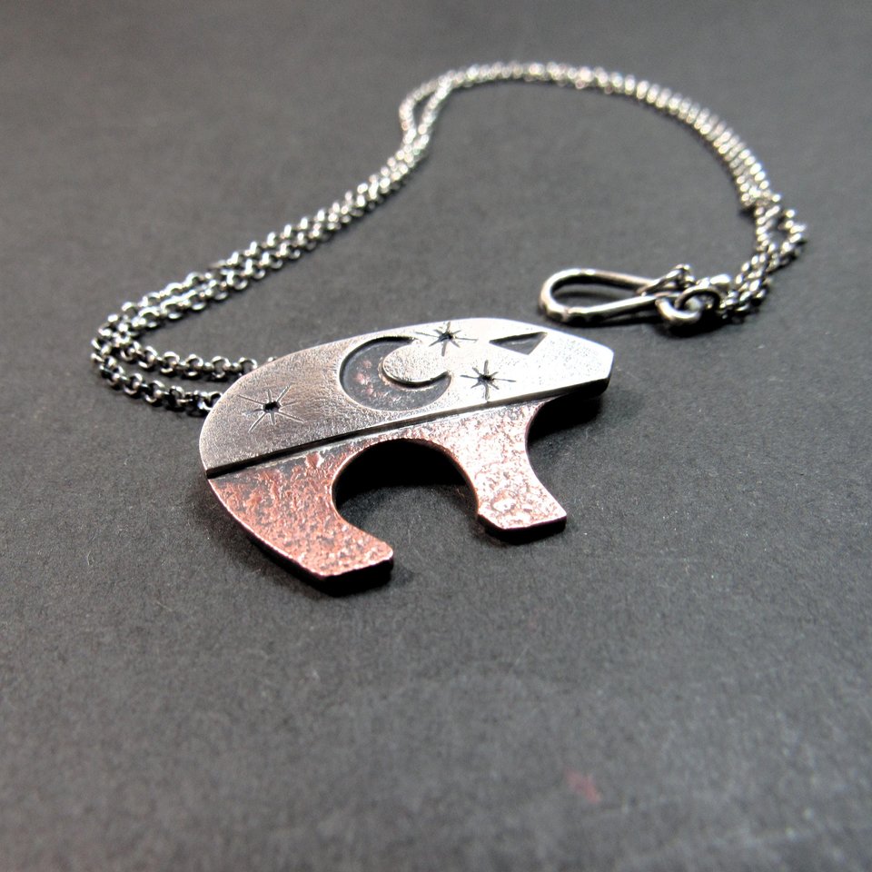 Celestial bear pendant inspired by the Ursa Major constellation, combining polished sterling silver and warm oxidized copper, featuring moon and star details that allow the copper to peek through the silver.  18 inch SS cain and findings complete the bear pendant necklace. Displayed on grey background.