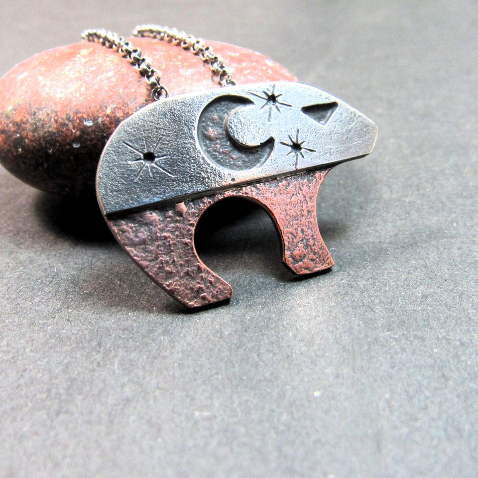 Mixed metal bear pendant with sterling silver top and solid copper bottom, showing a crescent moon and star sky design, rustic hammered texture, and strong contrast finish, measuring 3/4 inch tall by 1.25 inches long. 18" sterling silver chain with handmade findings. Displayed against rock and grey background.