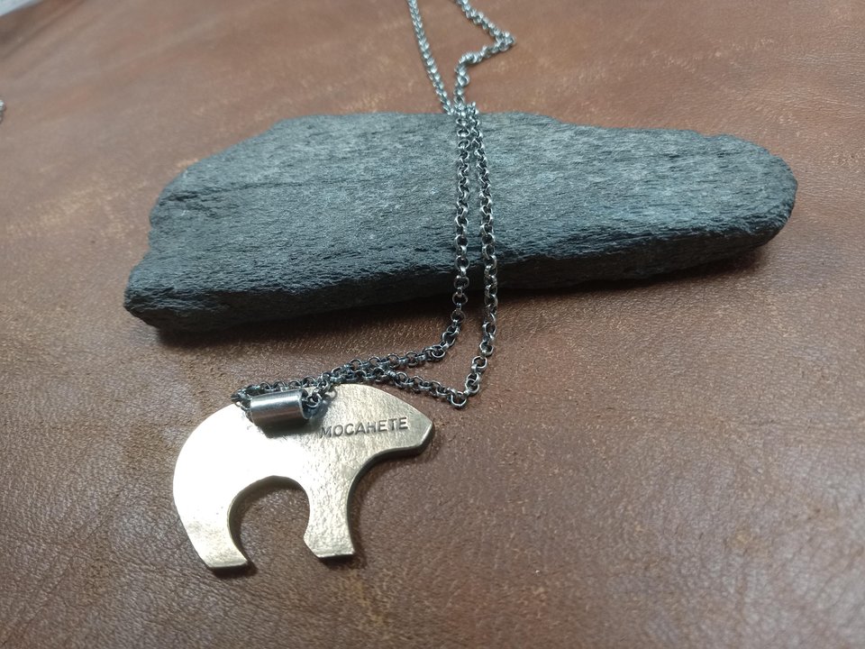 Reverse side of bear pendant by Mocahete showing makers mark. Rock and leather background.