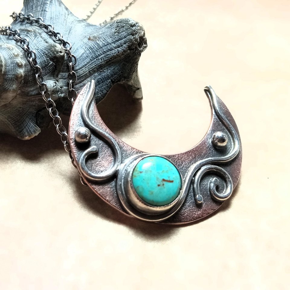 Side view o fcopper, silver and turquoise moon pendant showing details. Photo against shell and beige background.