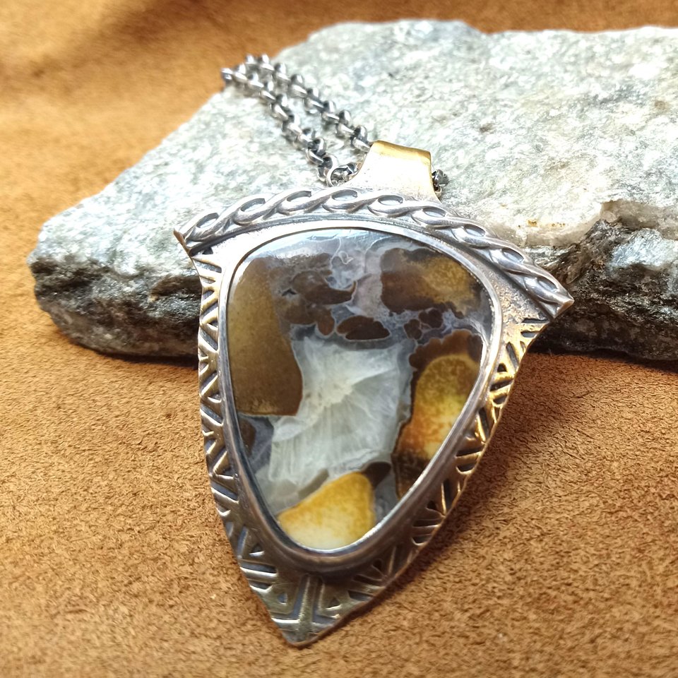 Cobra jasper, bronze and sterling silver pendant by Mocahete, photographed against a rock on leather.