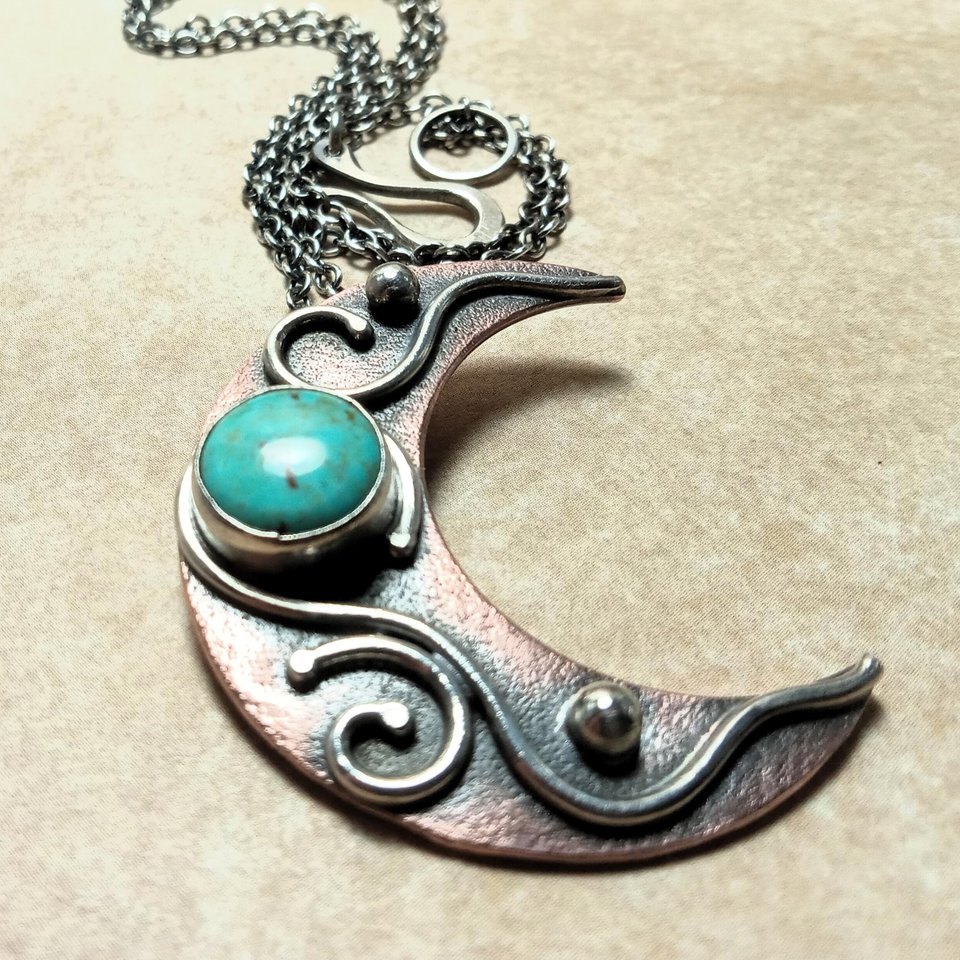 Moon pendant by Mocahete with turquoise, copper and silver showing clasp and chain on beige background.