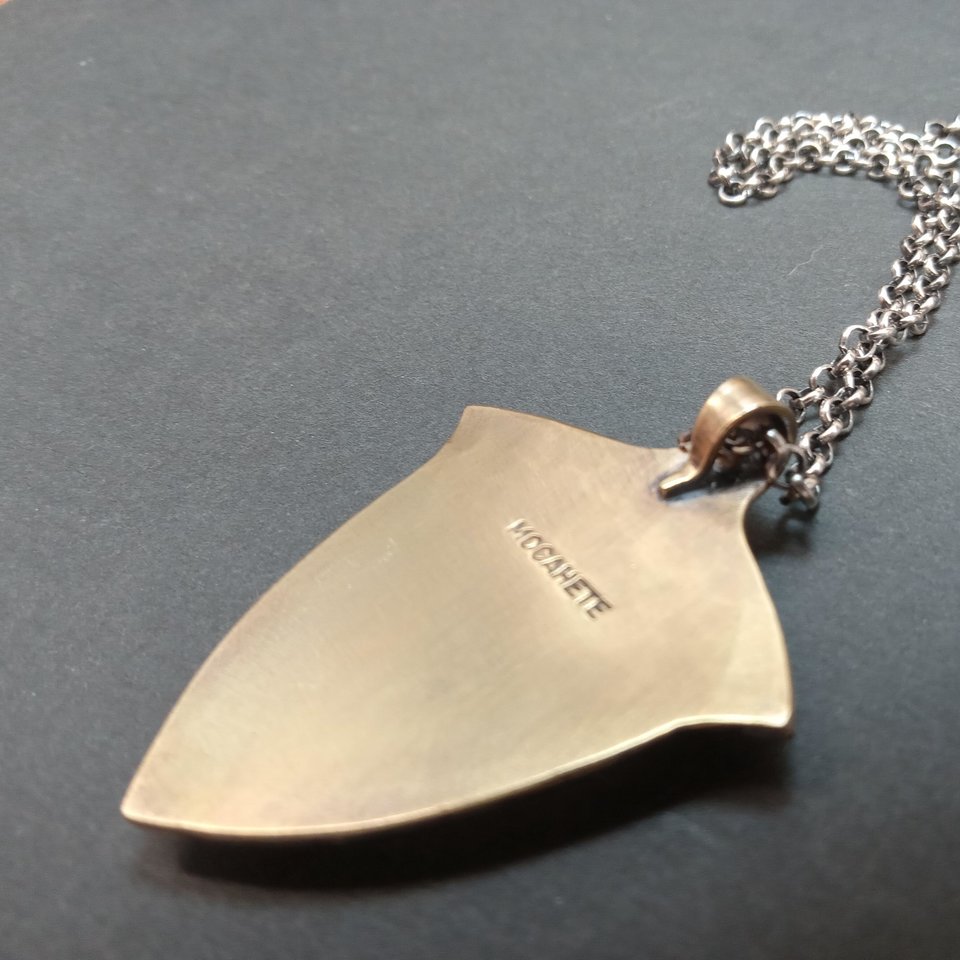 Reverse side of cobra jasper pendant showing the Mocahete makers mark, photo on dark background