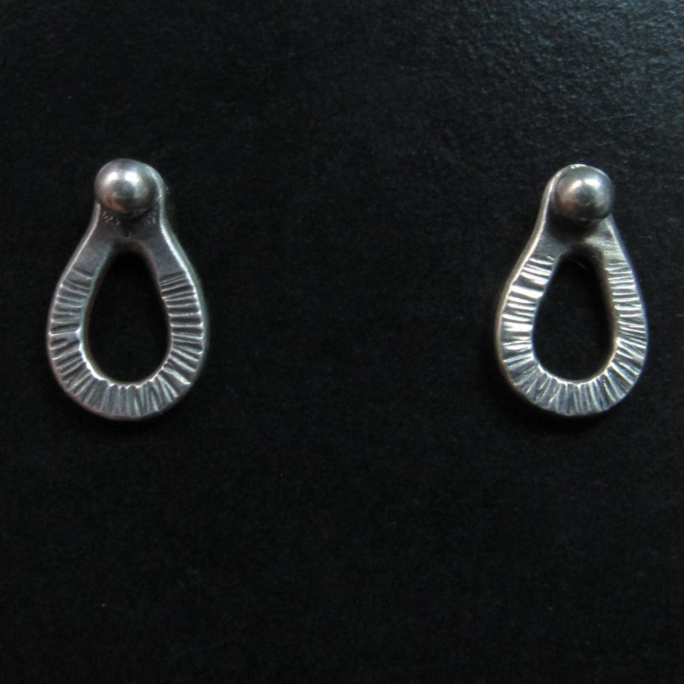 Sterling silver post back or stud earrings shaped like a raindrop and textured. A small orb of silver at the top is the crowning touch. Earrings measure 1/2" long and 1/4" wide. Comes with SS backs not pictured here.Displayed on black background with earrings facing forward.