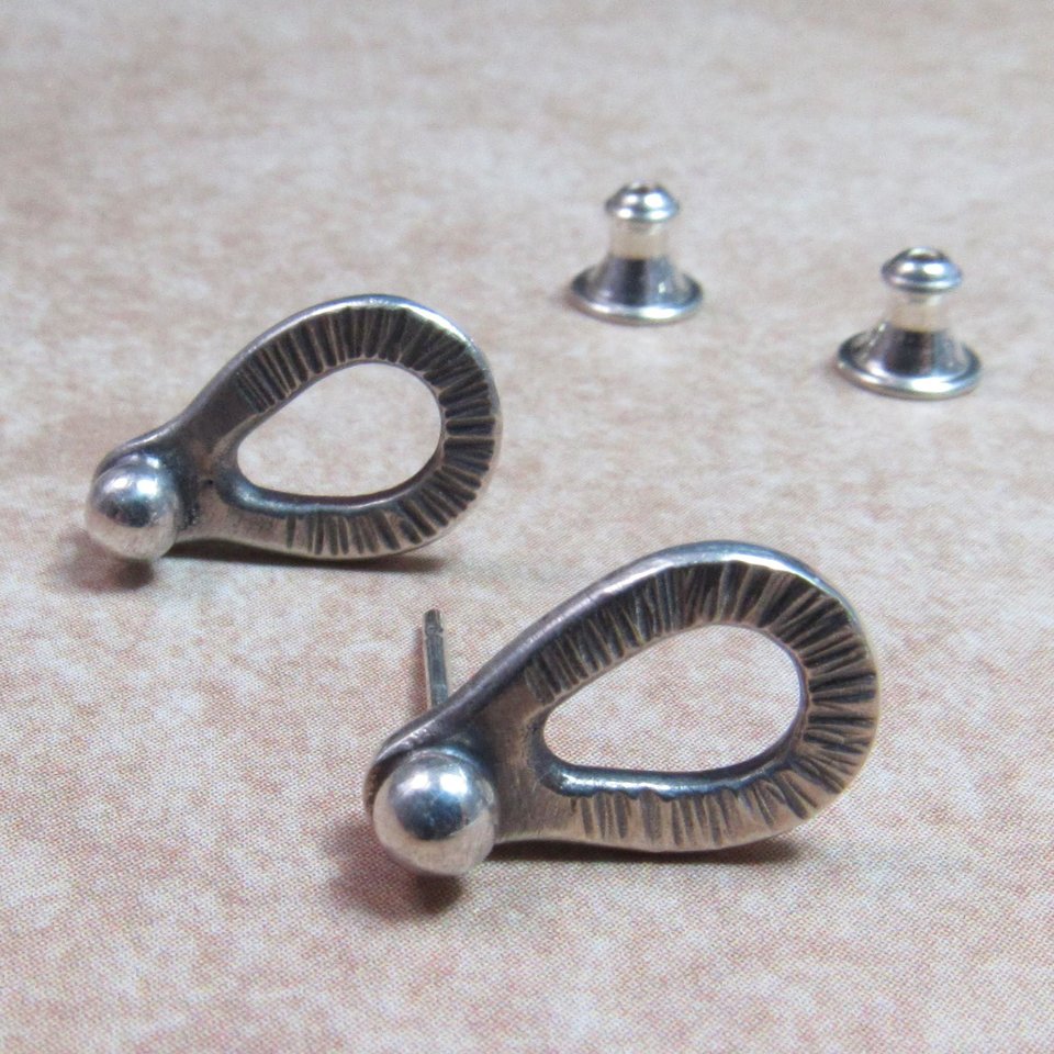 Sterling silver post back or stud earrings shaped like a raindrop and textured. A small orb of silver at the top is the crowning touch. Earrings measure 1/2" long and 1/4" wide. Comes with SS clutch backs.Displayed on light background.