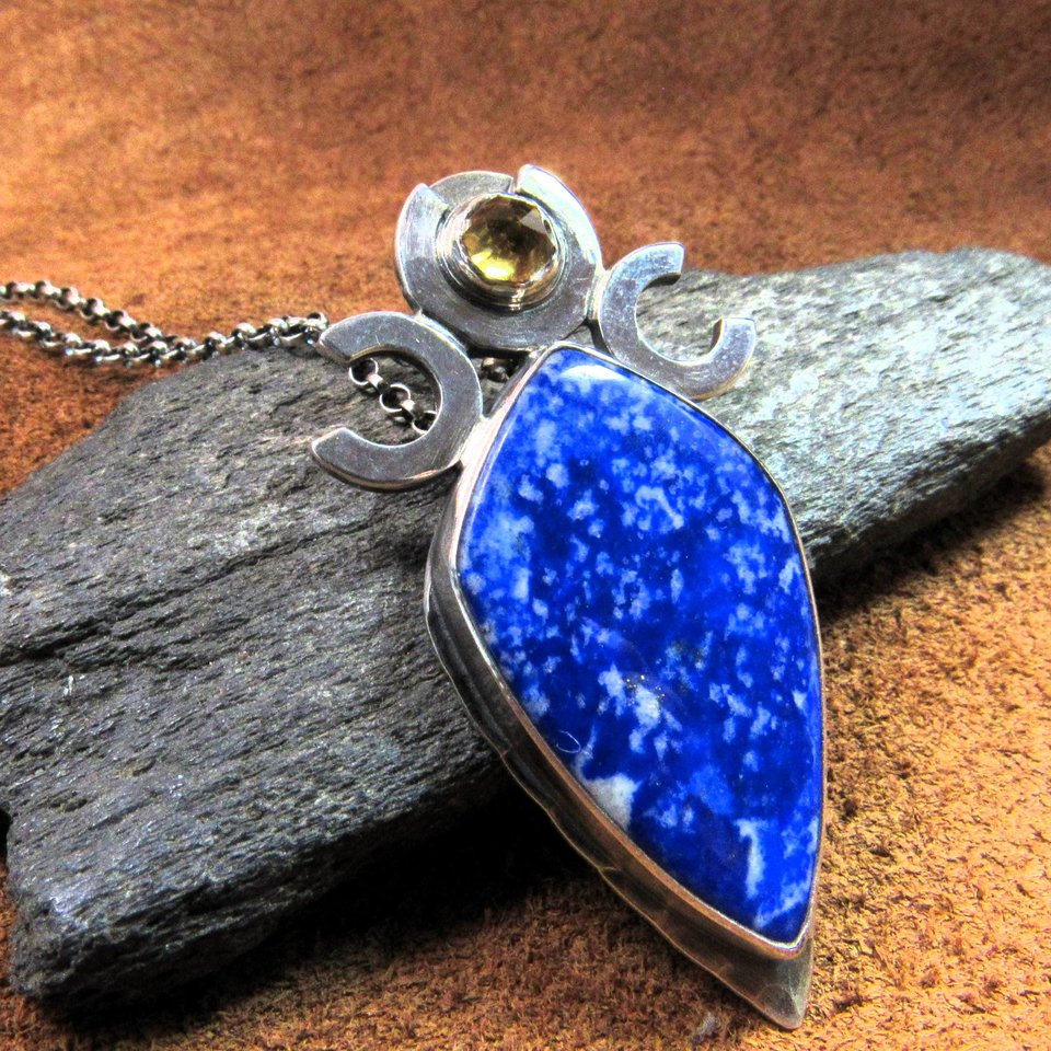 Triple goddess / moon pendant necklace with a faceted citrine and large lapis lazuli cabochon crafted from argentium sterling silver, fine silver. Pendant measures 2 inches from the top and is 7/8 inch across widest part and is suspended on a 18 inch sterling silver chain. Displayed against dark rock on brown leather.