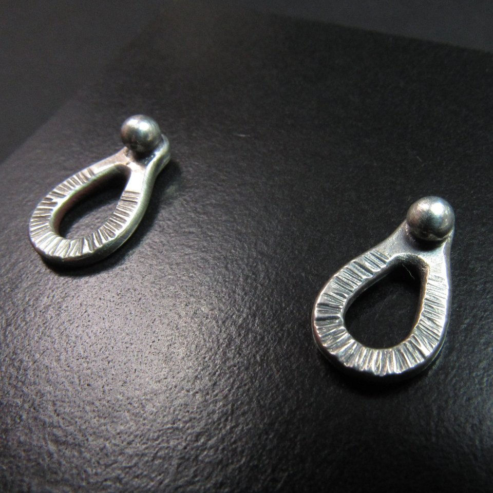 Sterling silver post back or stud earrings shaped like a raindrop and textured. A small orb of silver at the top is the crowning touch. Earrings measure 1/2" long and 1/4" wide. Comes with SS backs not pictured here.Displayed on black background.