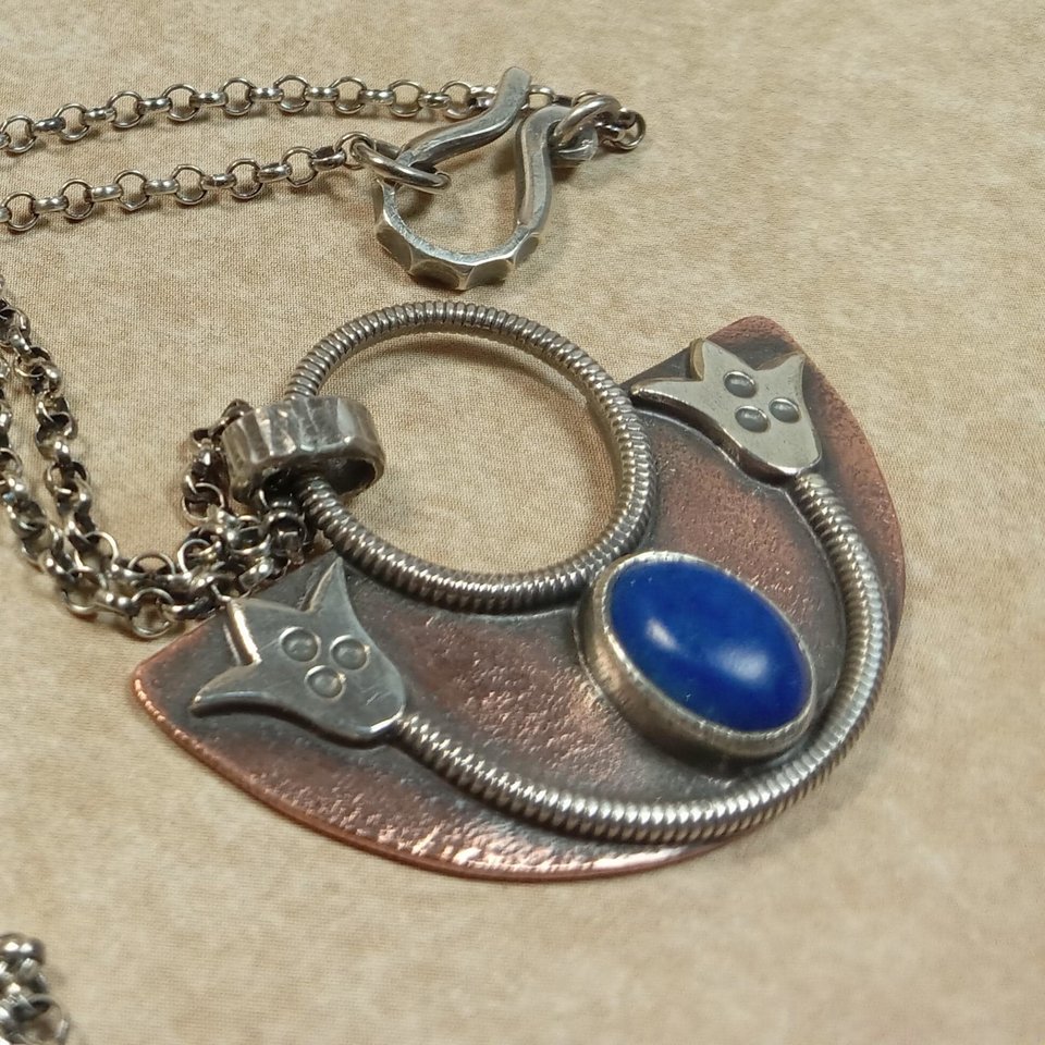 Up close photo to show details of Handcrafted mixed metal lotus pendant in argentium silver and copper with lapis lazuli cabochon. Displayed on neutral background.