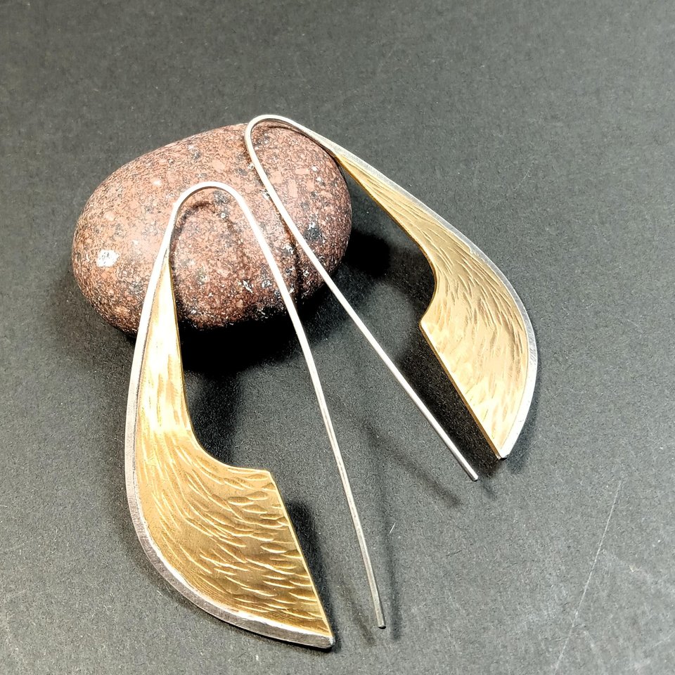 Sword like earrings measure  2.25" tall x .75" wide. Handmade from mixed metals of bronze and silver. Displayed against rock on dark background.