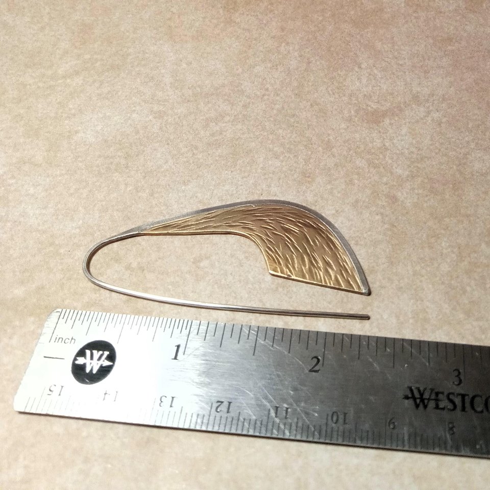 Sword shaped handcrafted earrings in bronze and silver. 2.25" tall x .75" wide, displayed against ruler on neutral background.