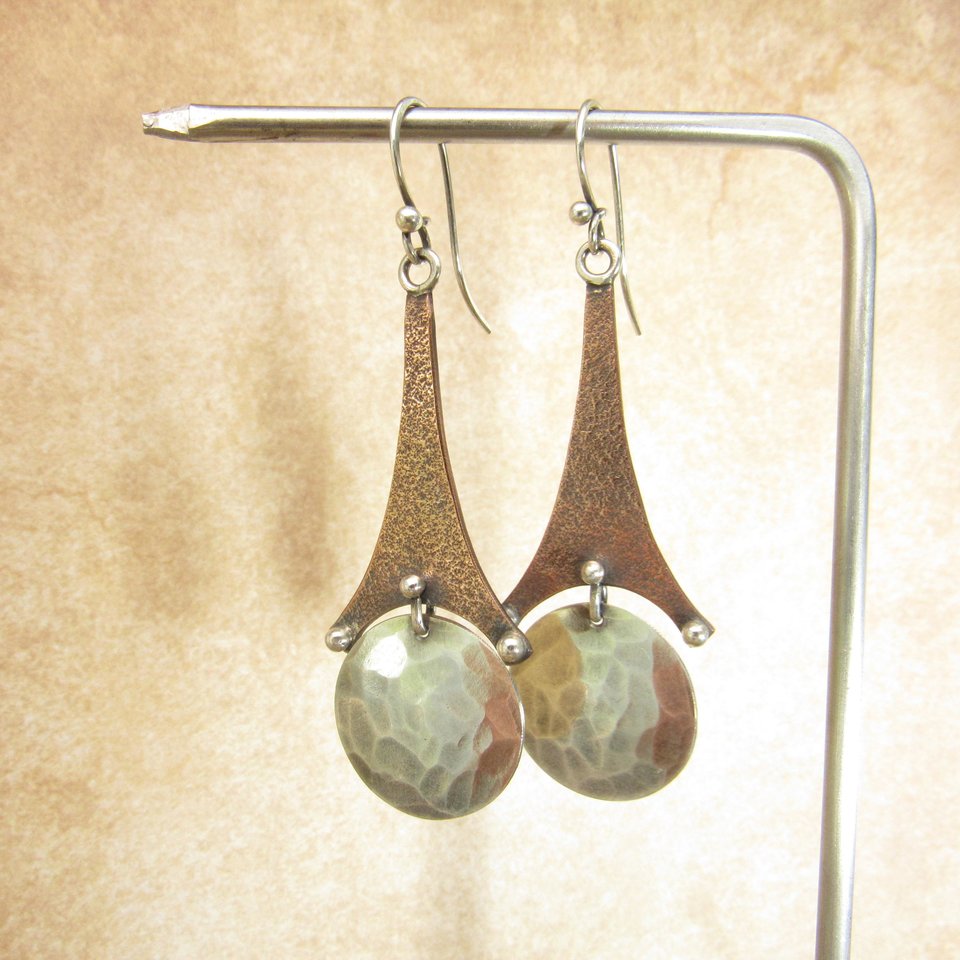 Copper And SS long earrings with disk. Displayed hanging from stand.