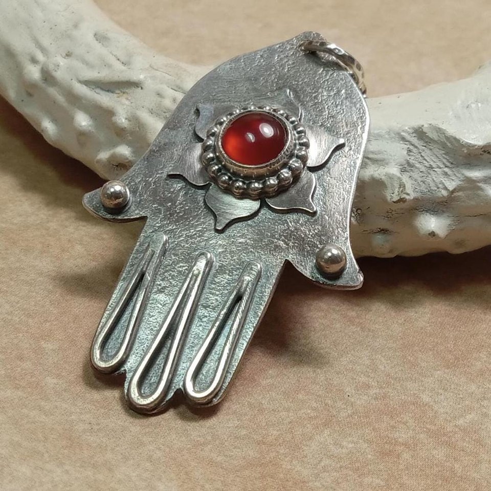 Slight angled view of SS Hamsa with lotus flower motif and carnelian. Displayed against white antler on neutral background.