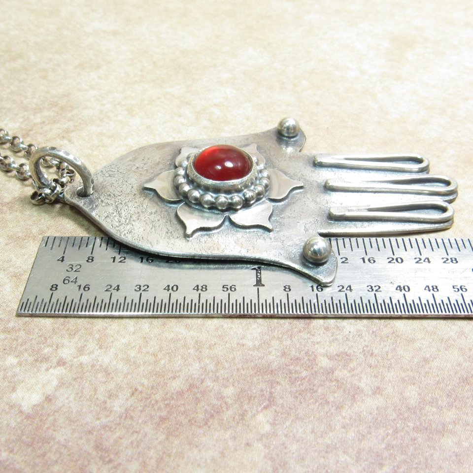 SS Hamsa displayed against ruler on neutral background. Pendant measures apx. 2" long.