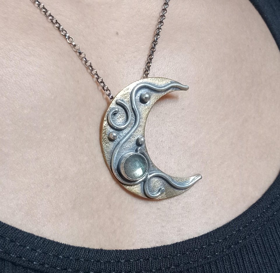 Crescent moon pendant in bronze and silver with labradorite cabochon. Shown being worn on a person with black tank top.