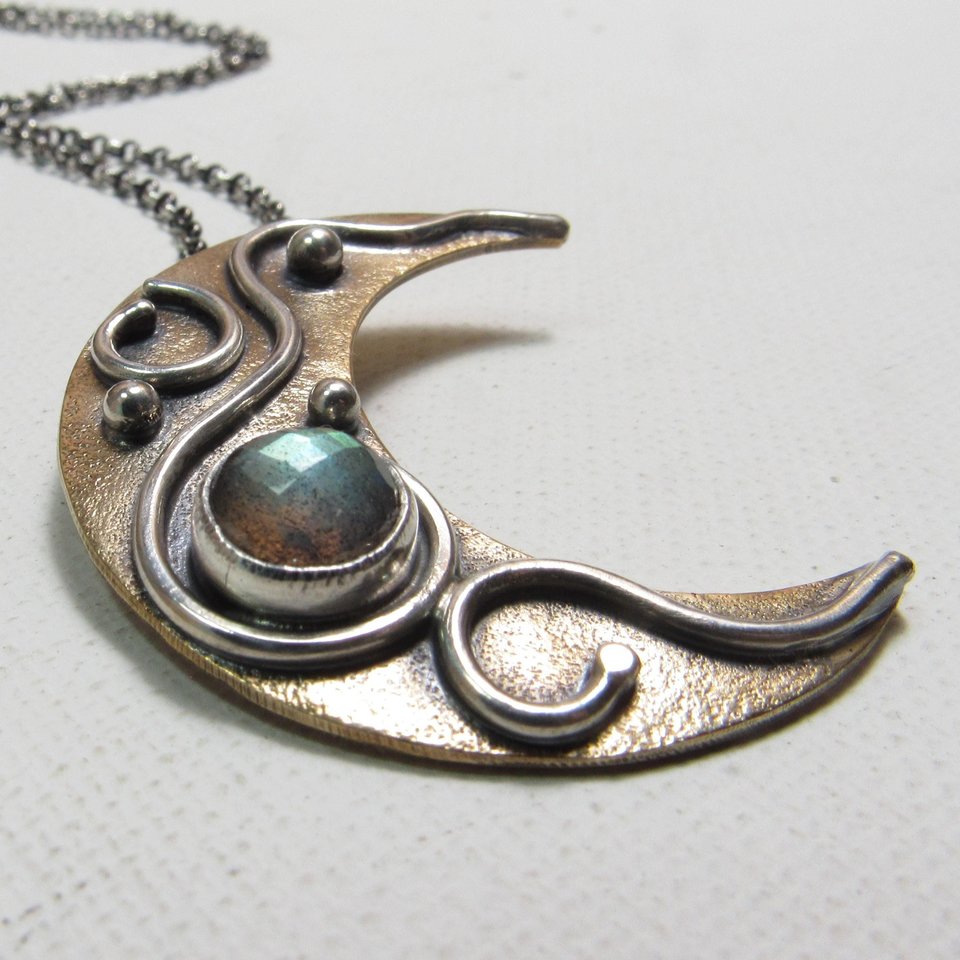 Mixed metal, bronze and argentium SS moon pendant with faceted labradorite cab. Displayed on white background.