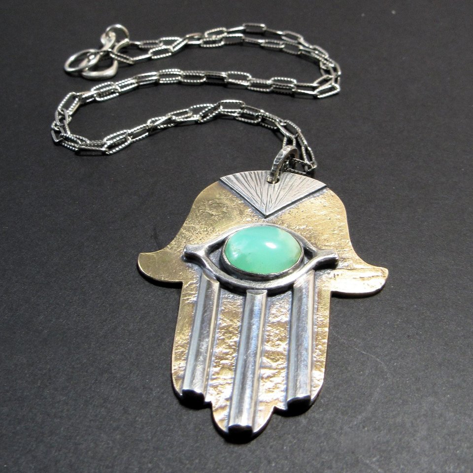 Close up of hamsa pendant necklace showing chain detail. Displayed on dark grey background