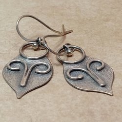 Argentium silver dangle earrings in a mask shape with wire embellishment. Displayed on neutral background.