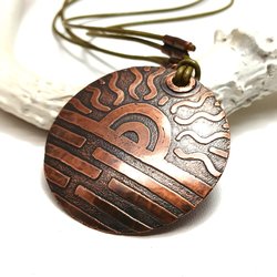 Etched copper pendant with sun design on leather cord displayed against white antler and white background.
