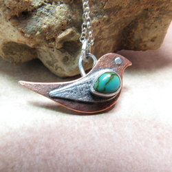 Mixed metals, copper and silver along with turquoise make up this little bird pendant necklace suspended on 18" SS chain. Displayed on neutral background with rock.