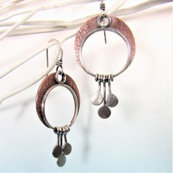 A lovely pair of mixed metal crescent moon earrings with moving paddles hanging from the crescent. Argentium silver and copper, 2 inch long, 1 inch wide. Swingy movement and lightweight. Perfect for dancing all night. Oxidized, polished, lovely glow. Displayed against white twigs on blue paper.