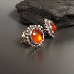 A pair of silver earrings with round amber cabochon set in a beaded bezel. Displayed against black rock and grey background.