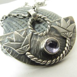 A striking and unusual lotus pendant necklace with an Egyptian theme and a lovely bezel set violet iolite. Pendant measures 7/8 inch tall and 1 and 3/8 inch wide. Fan shape with double lotus design. 18 inch SS chain and handmade findings.