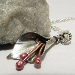 A silver and copper pendant necklace with a lily flower design. The flower is made of silver and has three copper stems with pink tips. The necklace is attached to a silver chain with silver clasp.