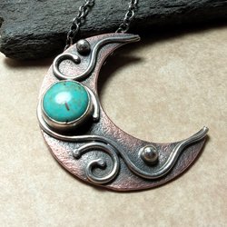 Close up of copper and silver moon pendant with turquoise cabochon, photo against rock on beige background.