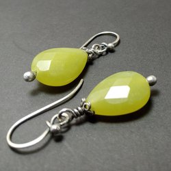 Close-up of handcrafted green faceted serpentine teardrop earrings with sterling silver bead and cap accents, hanging from artisan-made Argentium ear wires on a dark background.