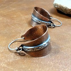 Two tone mixed metal basket shaped hoop earrings in copper and sterling silver. The textured copper hoops are encircled with a floral pattern sterling silver wire and SS ear wires. Displayed on light brown back ground with white rock.