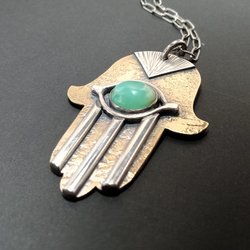 Large mixed metal Hamsa pendant necklace in bronze and silver with green chrysoprase cabochon. Displayed on dark grey background.