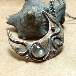 Bronze and sterling silver crescent moon pendant with bezel set labradorite cabochon.Displayed against black shell on neutral background.